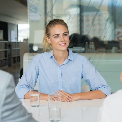 Portrait of beautiful young woman sitting in front of manager and senior leader during a job interview. Senior business people in conversation with a young business woman.  Recruiter checking the candidate during job interview.